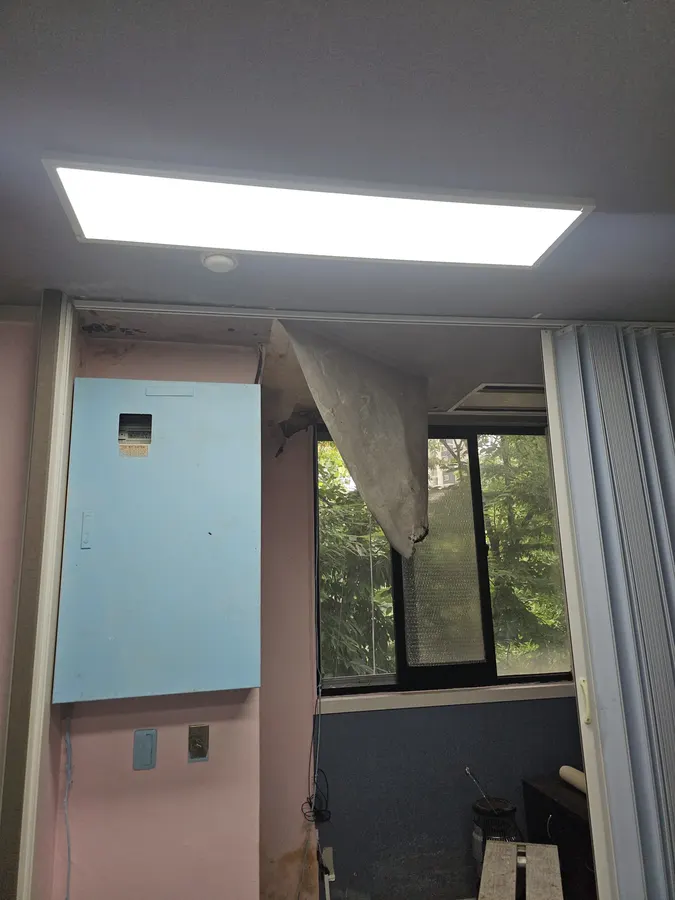 천장 일부가 늘어져 종이처럼 떨어지는 마감과 평판 조명이 보이는 상가